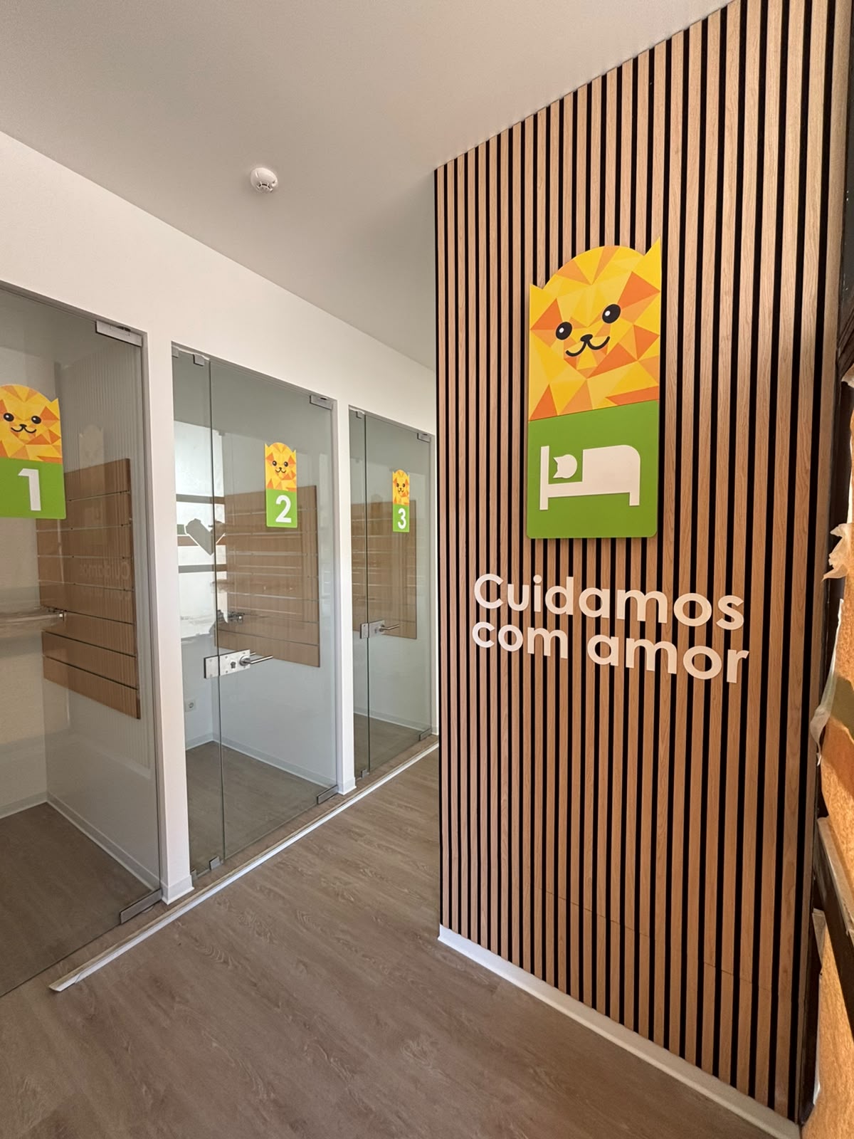 Entrada do hotel com suites de porta de vidro numeradas e parede de madeira com a frase Cuidamos com amor